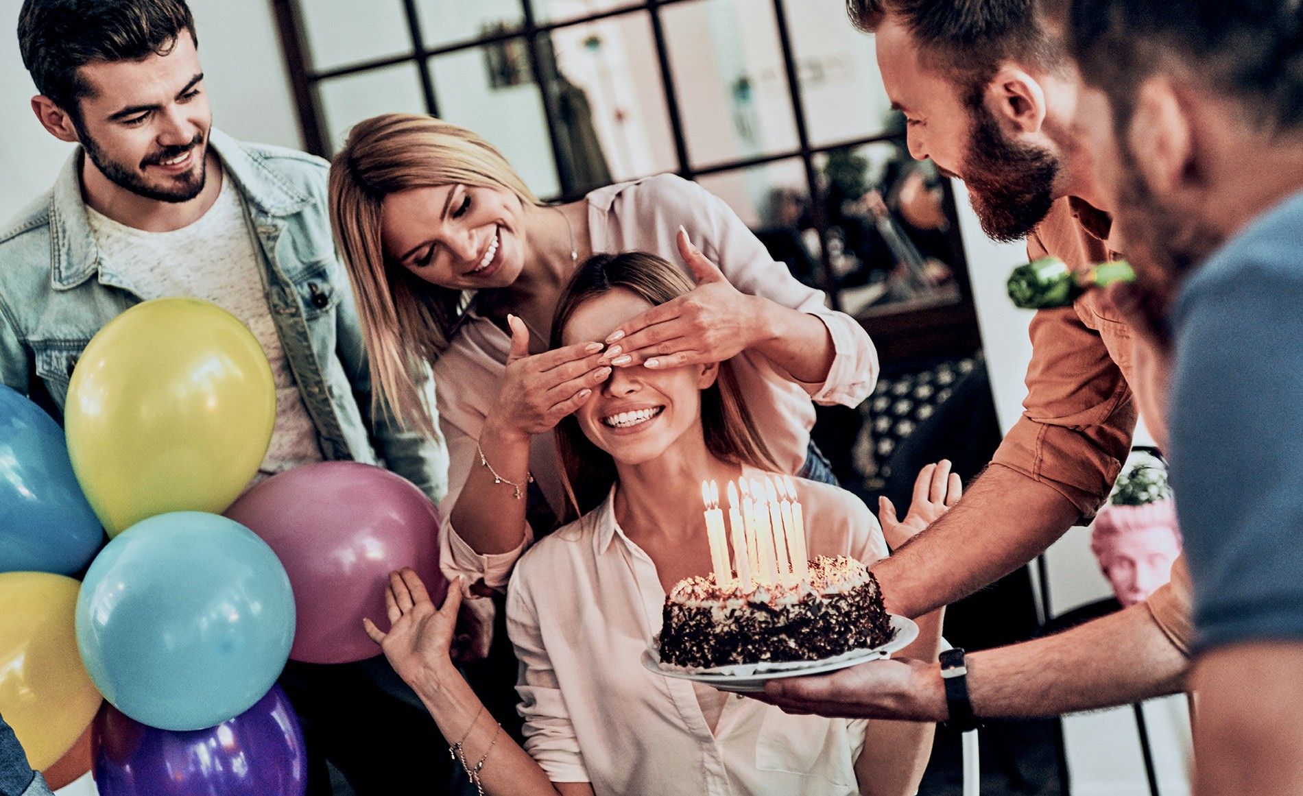 Amis organisant un anniversaire surprise avec gâteau et ballons colorés (source: www.smartbox.com)